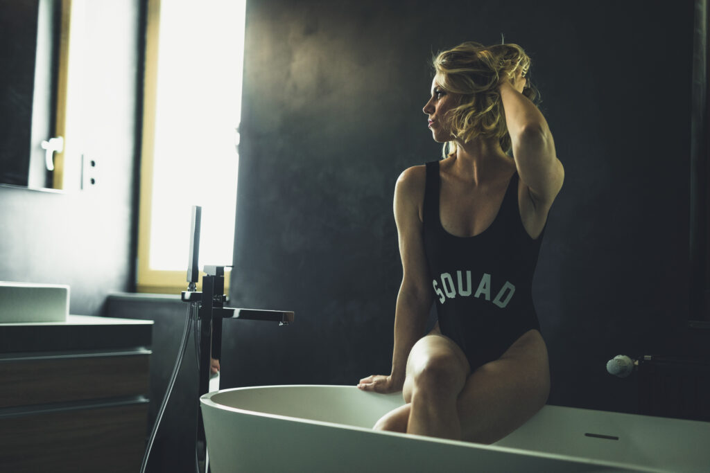 Eine Frau in einem stilvollen, modernen Badezimmer mit eleganter Wandgestaltung sitzt entspannt auf einer freistehenden Badewanne.