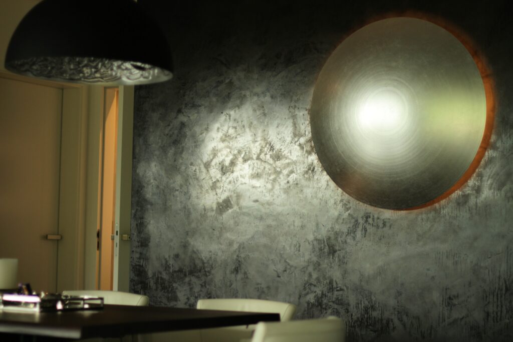 Ein stilvolles Wohnzimmer zeigt eine kreative Wandgestaltung mit Kalkputz und einem großen, kreisförmigen Kunstwerk.