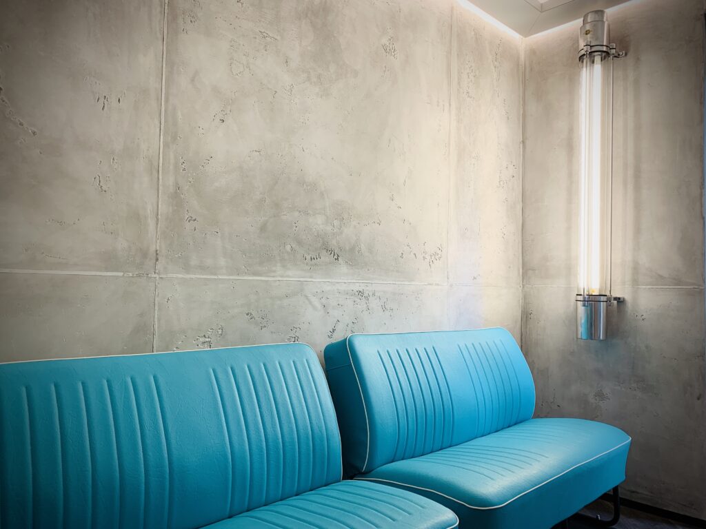 Ein modernes Wohnzimmer zeigt stilvolle Wände mit Oberflächen in Betonoptik und blauen Sofas zur Wandgestaltung.