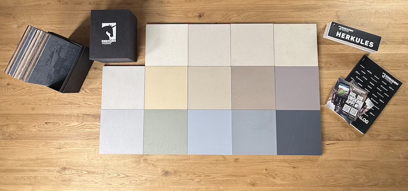 Eine „Best-of…-HERKULES-Musterbox“ zeigt verschiedene Farben für kreative Wandgestaltung auf einem Holzboden.