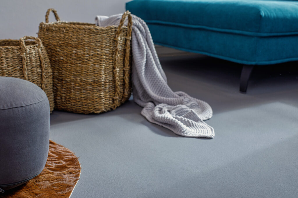 Ein stilvolles Wohnzimmer mit grauem Spachtelboden zeigt eine gemütliche Decke und Rattankörbe neben einem blauen Sofa.