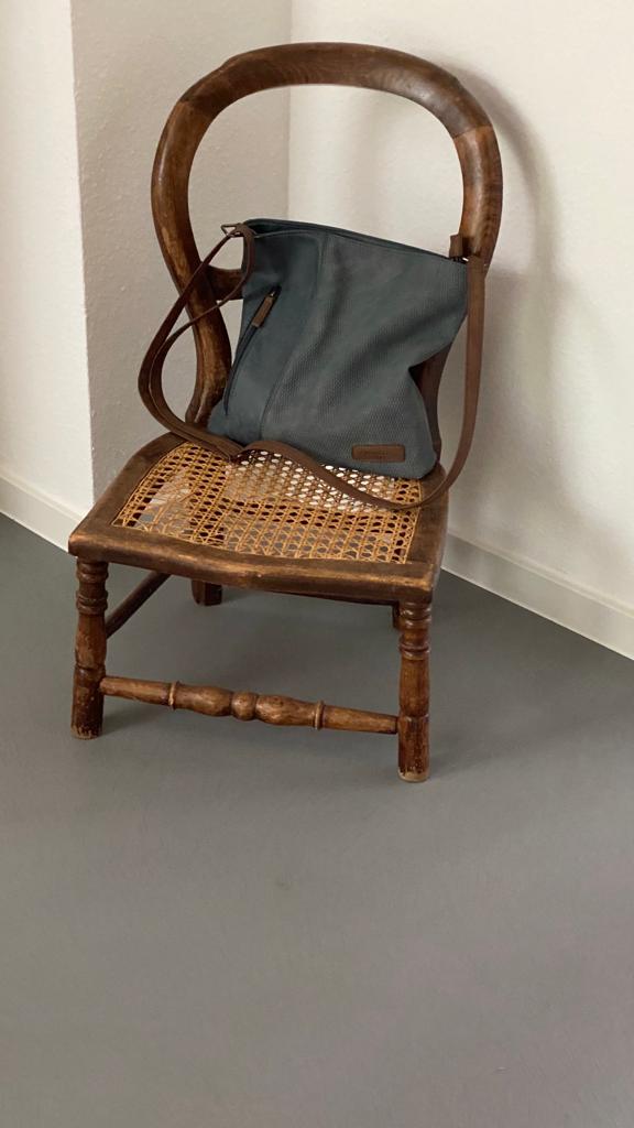 Ein eleganter Holzstuhl mit Tasche steht vor einer stilvoll gestalteten Wand im Wohnzimmer von Einhornwerke.