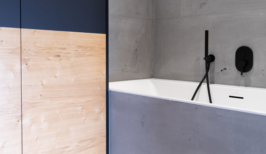 Eine moderne Badewanne in Betonoptik ergänzt die stilvolle Wandgestaltung im Badezimmer von Einhornwerke.