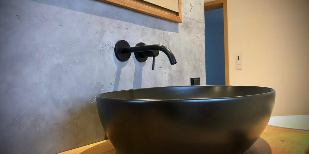 Ein modernes Badezimmer zeigt ein stilvolles schwarzes Waschbecken vor einer Wand in Betonoptik.