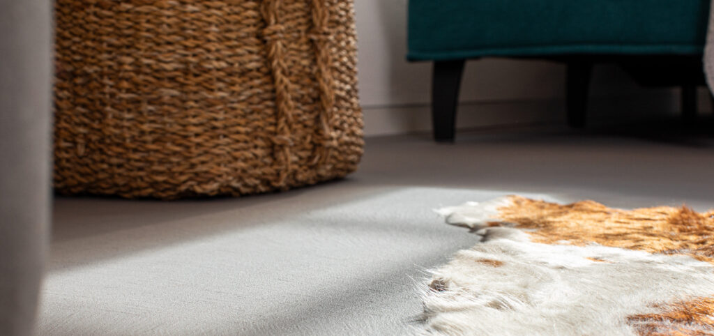 Ein stilvoller Betonoptikboden im Wohnzimmer wird durch einen geflochtenen Korb und einen Fellteppich akzentuiert.