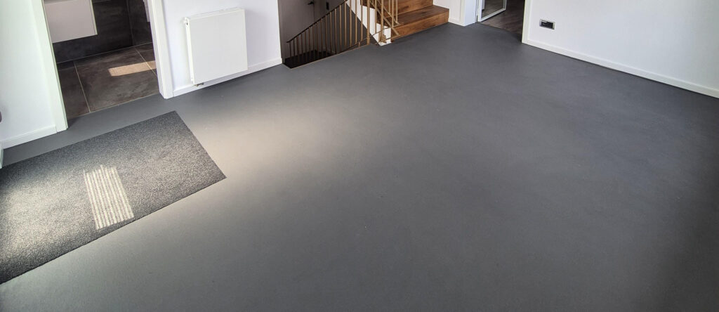 Ein Wohnzimmer mit modernem Betonoptikboden von Einhornwerke zeigt eine minimalistische Wandgestaltung.