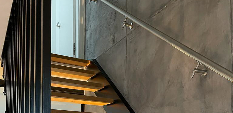 Ein modernes Treppenhaus mit Betonoptik-Wand und stilvollen Holzstufen zeigt kreative Wandgestaltung von Einhornwerke.