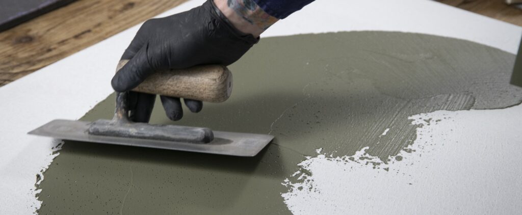 Ein Handwerker trägt STUCCORINO-Pigment mit einer Glättkelle auf eine vorbereitete Fläche für einen fugenlosen Boden auf.